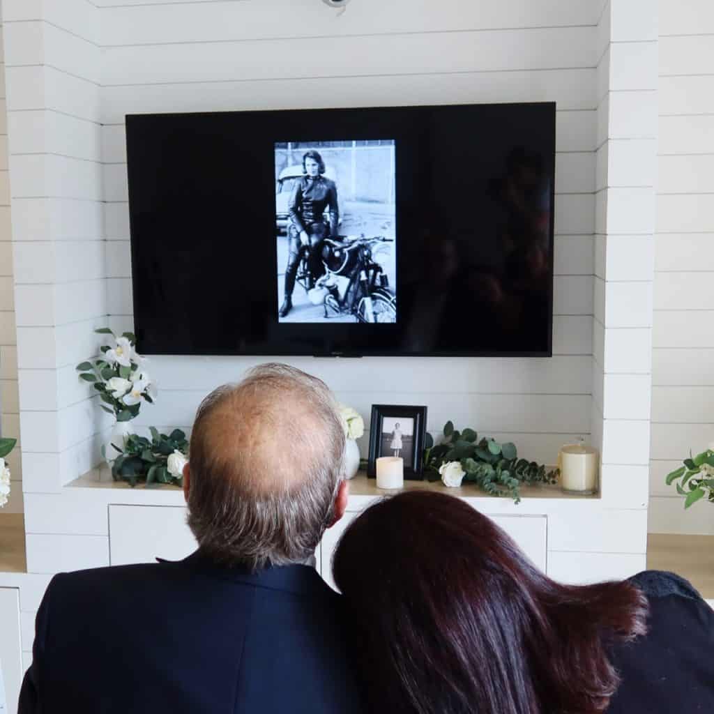Una pareja que observa una foto conmemorativa en una pantalla durante un funeral.