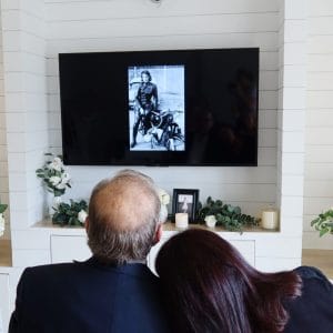 Couple viewing a memorial photo on a screen during a funeral service.