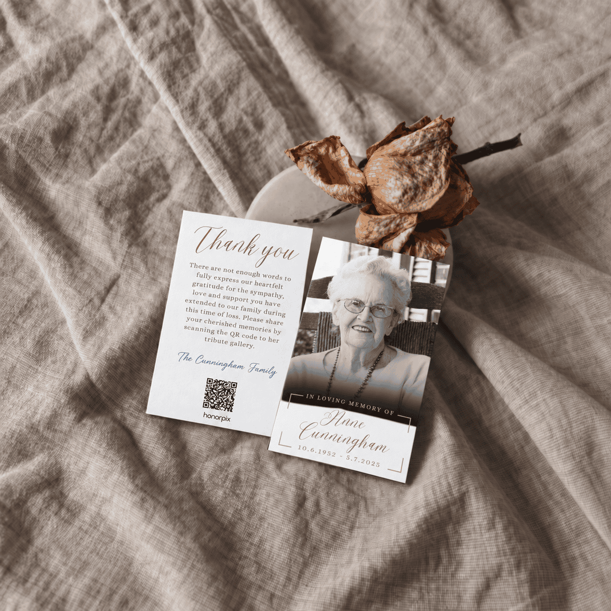 Memorial card with a photo of an elderly woman and a QR code on a beige fabric background.