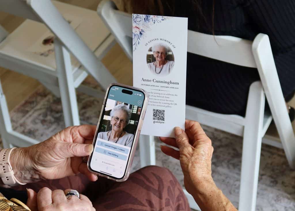 Person scanning memorial QR code on a tribute card with smartphone.