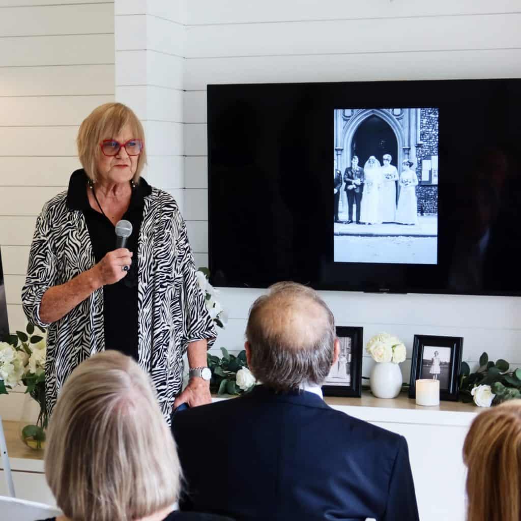 Woman giving a speech at a memorial service with a photo on screen.