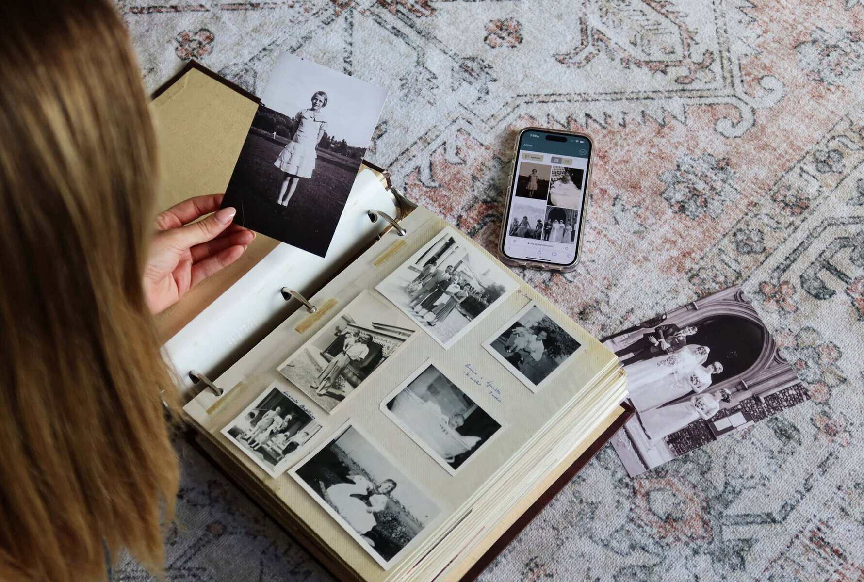 Person viewing a photo album with memorial photos and smartphone on a patterned rug.