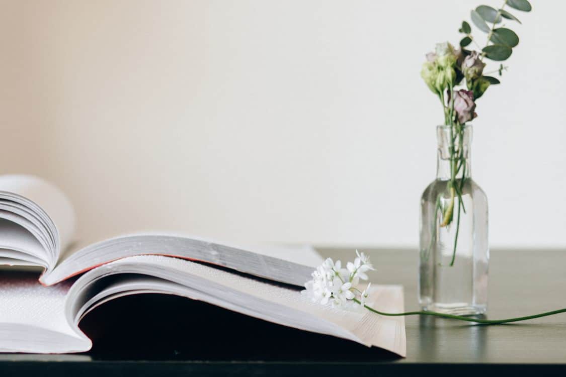An open memorial book resting beside a vase with delicate white flowers on a calm surface