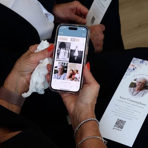 Person viewing memorial photos on smartphone during funeral service.