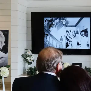 People viewing a memorial slideshow on a large screen at a funeral service.