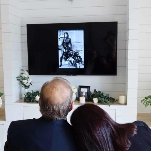 Couple viewing a memorial photo on a screen during a funeral service.